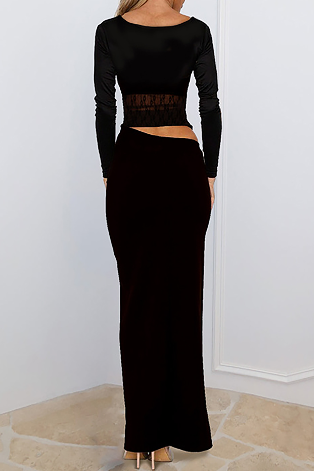 Woman wearing a black long-sleeved maxi dress with a lace inset bodice, holding a handbag.