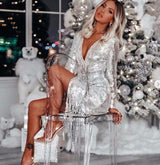 woman in a silver sequin dress with fringe detailing sitting on a clear chair