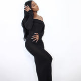 Woman wearing a long black off-the-shoulder dress with long sleeves, posing with her hand on her head against a white background.