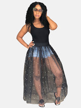 Woman wearing a black tank top and a black sheer maxi skirt with white pearl embellishments over denim shorts.