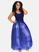 Woman wearing a navy tank top and a navy sheer maxi skirt with white pearl embellishments over denim shorts.