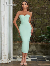 Front view of a woman wearing a light green strapless midi dress with a sweetheart neckline and corset-inspired bodice, standing in a garden setting.