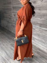 Woman in a rust-colored maxi dress with batwing sleeves, cinched waist, and side slits.