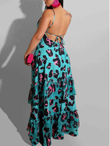 Back view of a woman wearing a turquoise maxi dress with a black and pink leopard print, showcasing an open back with tie closure and a tiered, ruffled skirt.