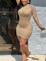 Full-body shot of a woman in a sparkling mini dress with a high neckline and long sleeves, holding a silver clutch.