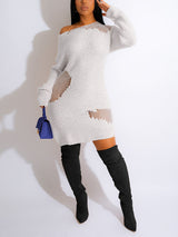 woman wearing a white distressed knit mini dress with an off-the-shoulder neckline and long sleeves, with black knee-high boots and a blue handbag
