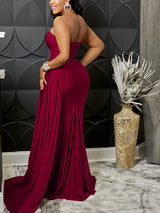 Rear view of a woman wearing a burgundy one-shoulder formal gown with a thigh-high slit and mermaid hemline.