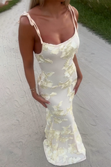 Full body shot of a woman wearing a cream floral appliqué evening gown with tie shoulder straps.