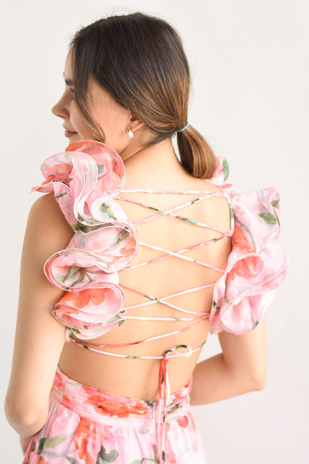 Close-up of the back of a pink floral print maxi dress, detailing the criss-cross lace-up closure and ruffled shoulder straps.