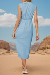 Back view of a woman in a light blue satin dress with a V-neck, collared neckline, sleeveless design, twisted front detail, and a high slit, standing in a desert landscape.
