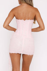 Back view of a woman wearing a pink strapless lace mini dress with a heart cutout on the bodice.