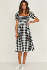 Woman wearing a black and white gingham check midi dress with puff sleeves and a square neckline, standing with her hand on her hip.
