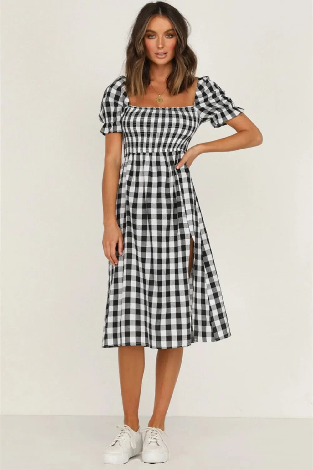 Woman wearing a black and white gingham check midi dress with puff sleeves and a square neckline, standing with her hand on her hip.