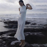 Woman wearing a white sleeveless ribbed knit midi dress with sheer panel detailing posing on rocks by the ocean