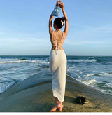 Rear view of a woman wearing a white knit midi dress with cut-out details and a small blue bag, standing by the ocean.