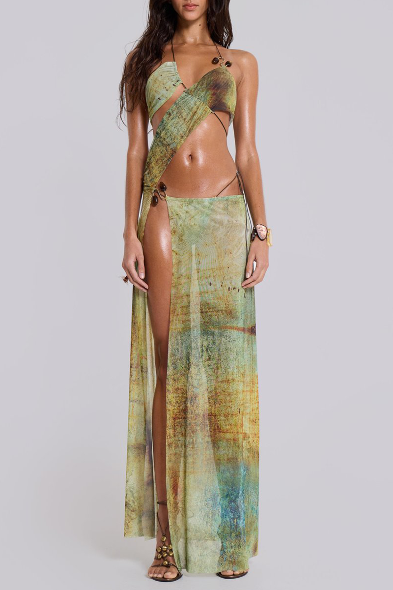 Woman wearing a green and brown abstract print halter neck maxi dress with a high slit and cut-out details.