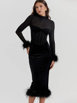 Woman wearing a black velvet midi dress with sheer long sleeves and feather trim