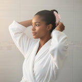 Woman in a white bathrobe using a pink claw clip to style her hair
