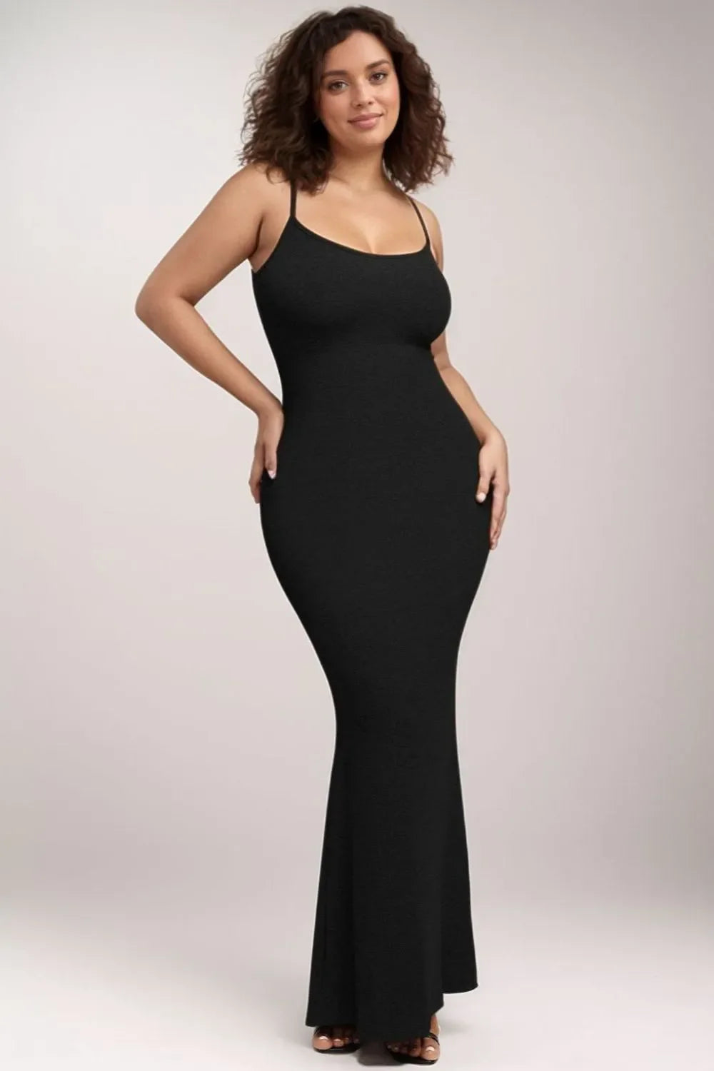 Woman in a long black ribbed knit dress with thin straps, hands on hips.