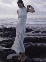 Woman wearing a white sleeveless ribbed knit midi dress with sheer panel detailing posing on rocks by the ocean