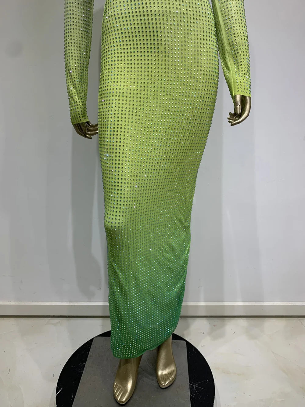Close-up of the lower portion of a gradient green, rhinestone-embellished dress on a mannequin.
