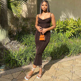 Woman wearing a brown ribbed knit bodycon midi dress with spaghetti straps and a cowl neckline, standing outdoors with greenery in the background.