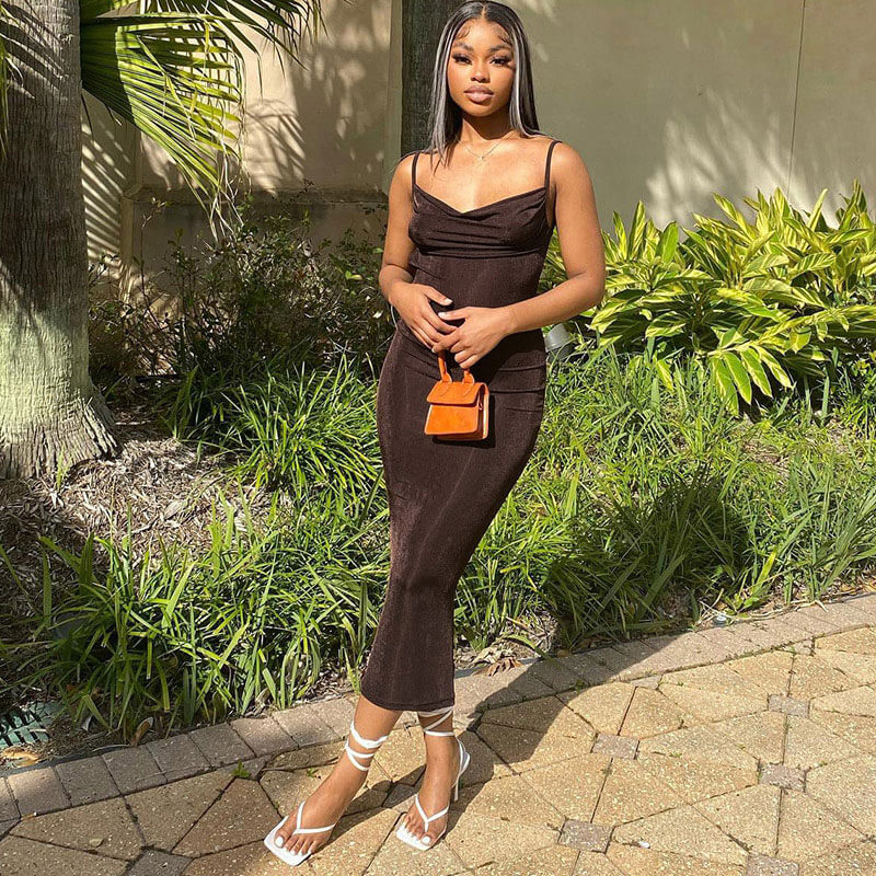 Woman wearing a brown ribbed knit bodycon midi dress with spaghetti straps and a cowl neckline, standing outdoors with greenery in the background.