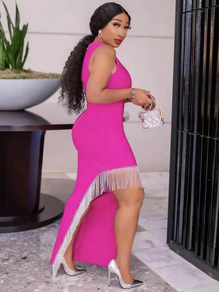 Side view of a woman wearing a bright pink sleeveless mock neck dress with a high slit and embellished trim, showcasing the dress's silhouette.