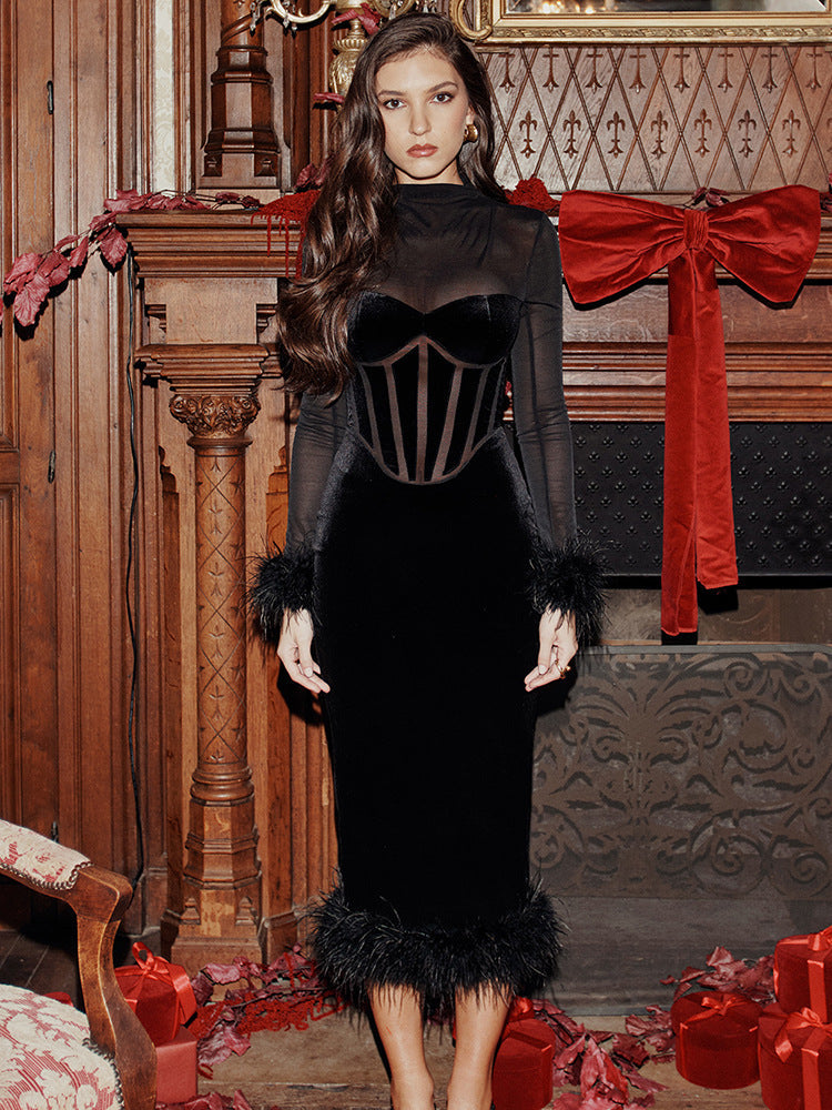 Woman in a black velvet dress with sheer sleeves and feather trim posing in a festive setting