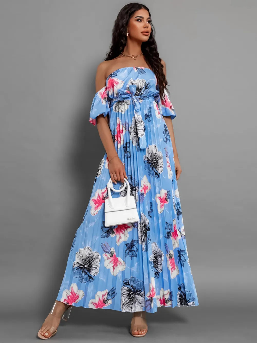 Full-length view of a woman in a blue floral off-the-shoulder maxi dress with pleats and puff sleeves.