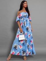 Full-length view of a woman in a blue floral off-the-shoulder maxi dress with pleats and puff sleeves.