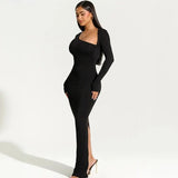 Woman posing in a black long-sleeved maxi dress with an asymmetrical neckline and a high slit.