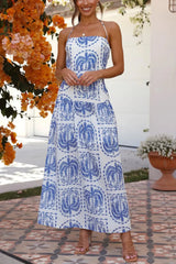 Woman wearing a white maxi dress with a blue palm tree print and halter neckline, standing outdoors