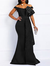 Front view of a woman in a black off-the-shoulder mermaid gown with lace bodice and pearl embellishments on the ruffle.