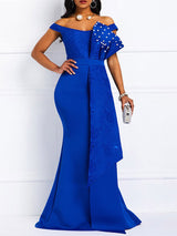 Front view of a woman in a royal blue off-the-shoulder mermaid gown with lace bodice and pearl embellishments on the ruffle.
