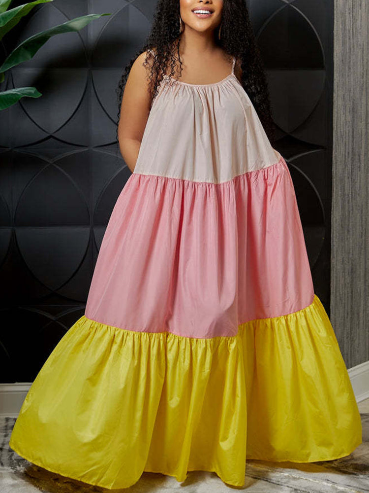 Woman wearing a long, tiered maxi dress with alternating panels of light pink, pastel pink, and yellow fabric. The dress has spaghetti straps and a gathered neckline.