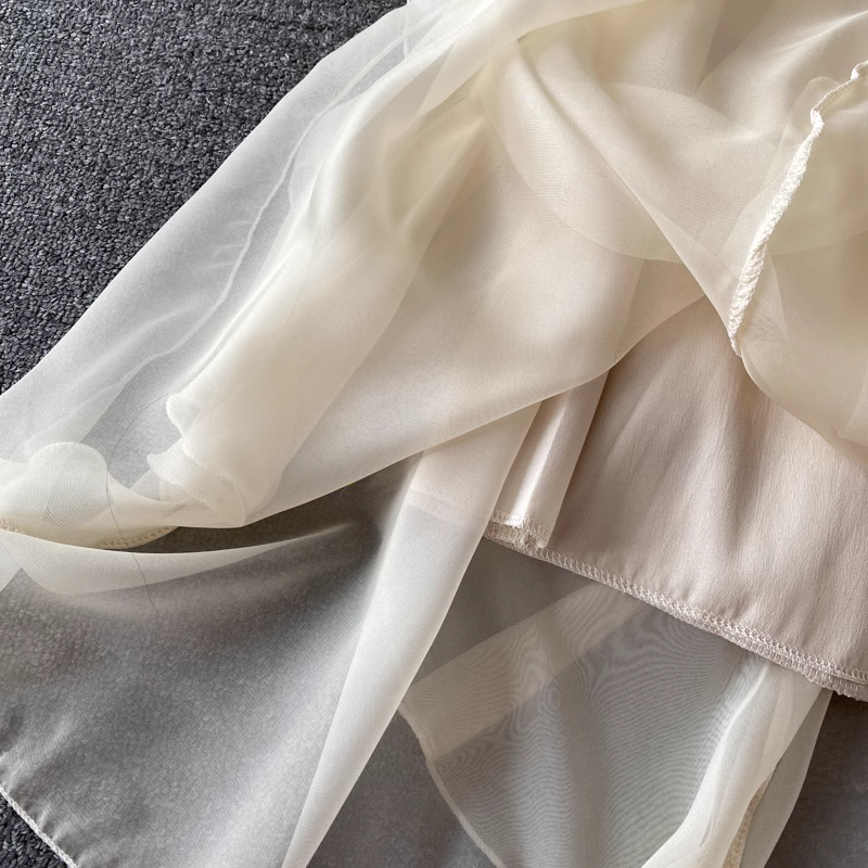 Close-up of the layered chiffon fabric of a cream-colored dress, showing the sheer overlay and satin lining.
