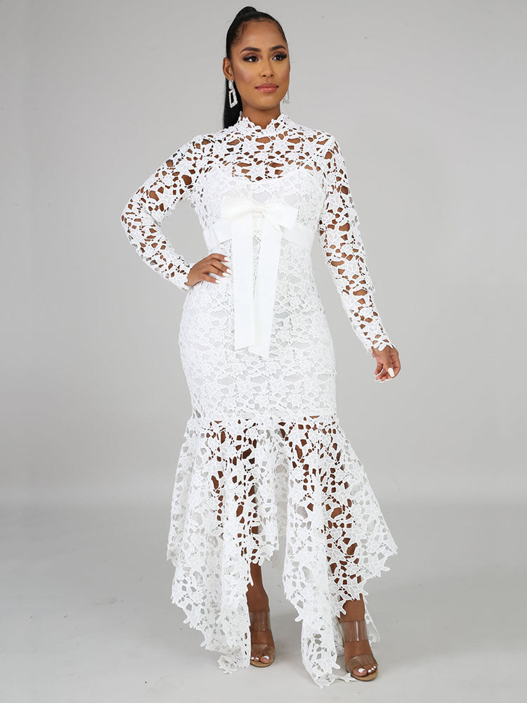Woman wearing a white long-sleeved lace mermaid dress with a high neckline and a sash, posing in a studio.