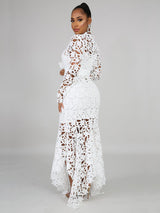 Back view of a woman in a white lace maxi dress with a high neckline and long sleeves.