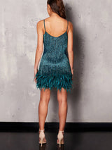 Back view of a woman in a teal sequined mini dress with fringe and feather trim.