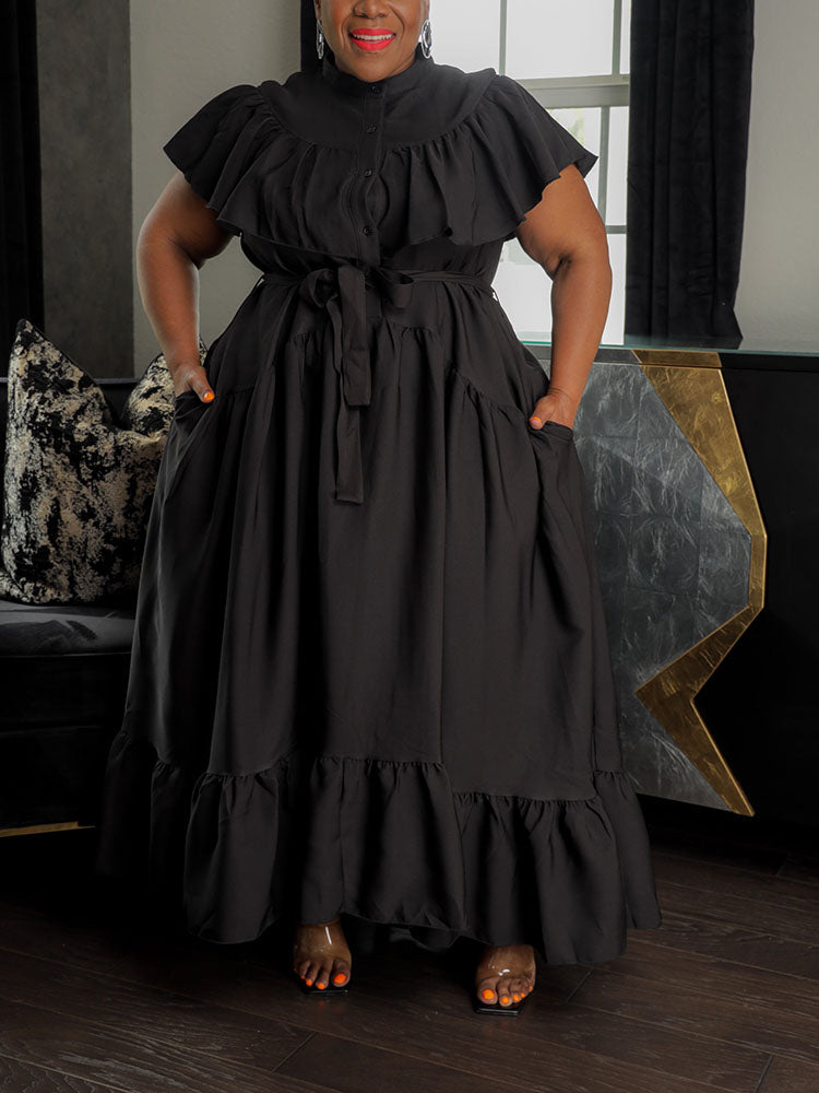 Woman wearing a black maxi dress with ruffled neckline and tiered skirt.