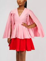Close-up of a woman's upper body in a pink and red color-block dress with cape sleeves, showcasing a necklace.
