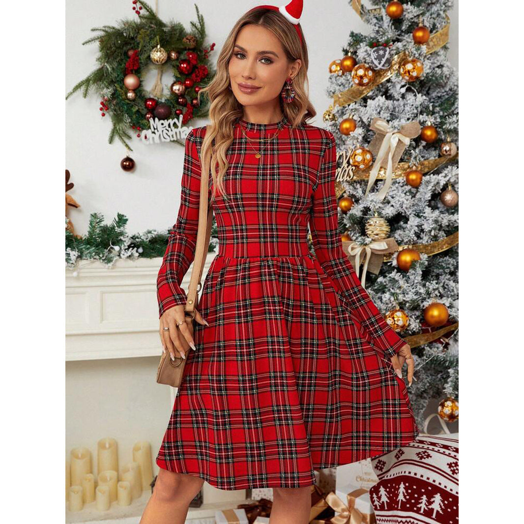 Woman wearing a red plaid long-sleeve fit and flare dress with a round neck, standing in front of a decorated Christmas tree.