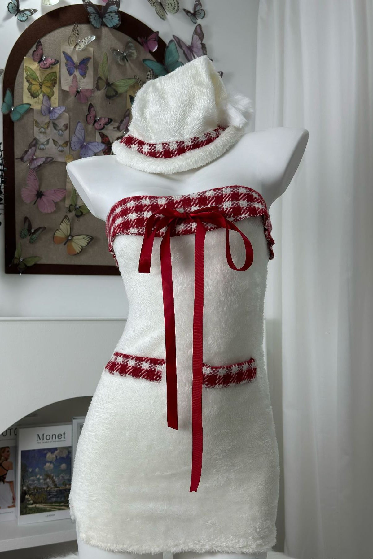 White strapless dress with red plaid trim and red ribbon accents, displayed on a mannequin with a matching hat.
