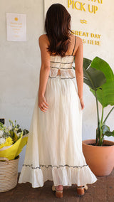 Back view of a woman wearing a white crinkle fabric two-piece set with black trim and tie details.
