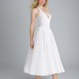 Side view of a woman in a white halter neck midi dress with a deep V-neckline and full skirt, against a gray background.