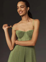 Close-up of a woman wearing a green pleated midi dress, showing the bodice detail and spaghetti strap.
