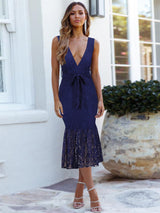 Woman wearing a navy blue lace midi dress with a deep V-neckline and a mermaid hem.