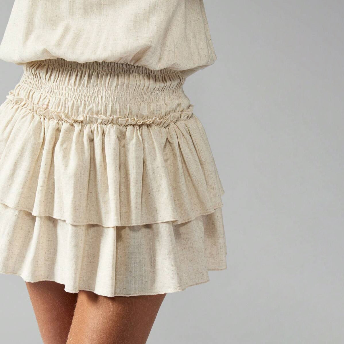 Close-up of the smocked waist and tiered skirt of a cream mini dress.