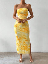 A woman models a yellow tie-dye print strapless maxi dress with a side slit.